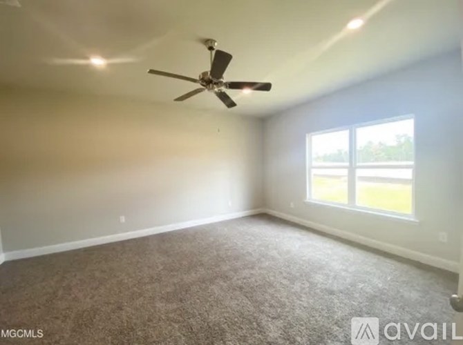 A room with a ceiling fan and a window overlooking a green area.