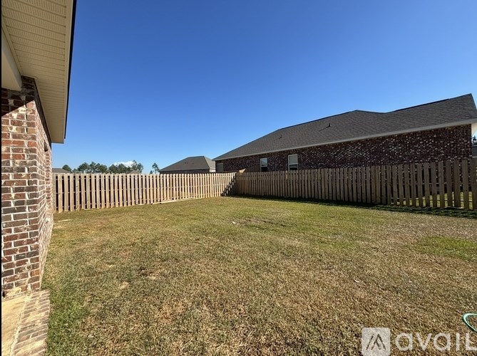 A grassy yard with a wooden fence and a house with a brick chimney.