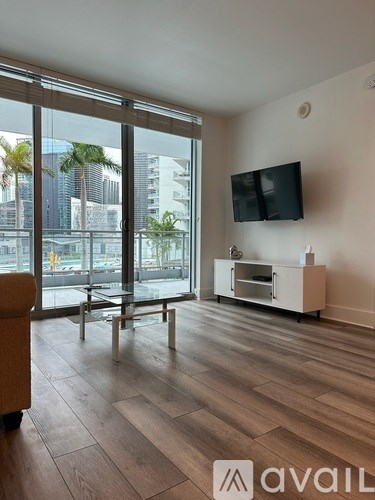 A living room with a flat screen TV mounted on the wall and a glass door leading to a balcony.
