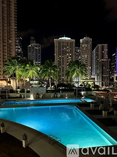 A pool at night with palm trees and buildings in the background.