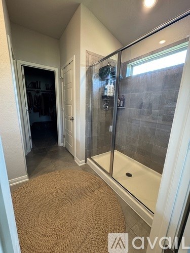 A bathroom with a glass shower door and a brown rug on the floor.