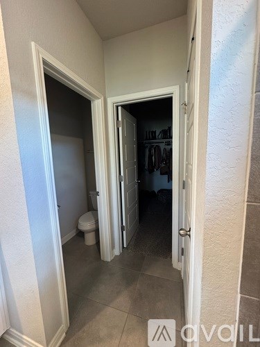 A hallway with a toilet and a door leading to a bedroom.
