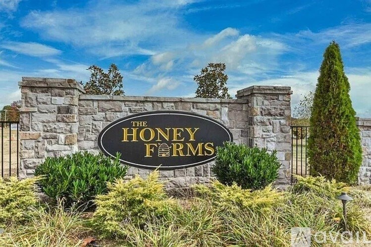 A sign that says "HONEY FARMS" is in front of a stone wall.