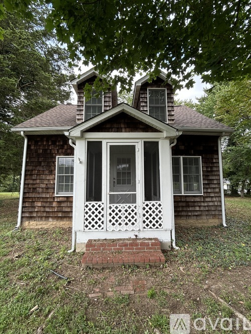 A small house with a porch and a brick base is surrounded by trees.