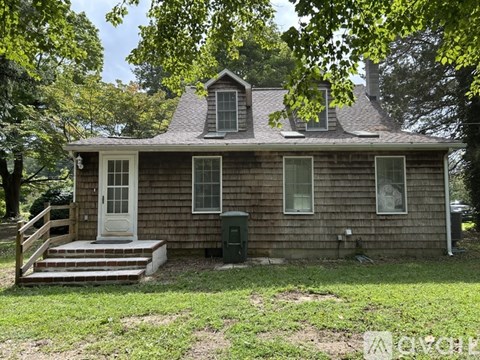 A small wooden house with a white door and windows surrounded by trees.