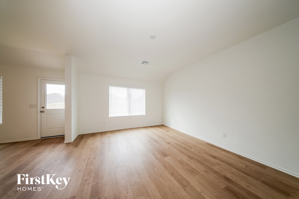 A spacious room with wooden flooring and two windows.