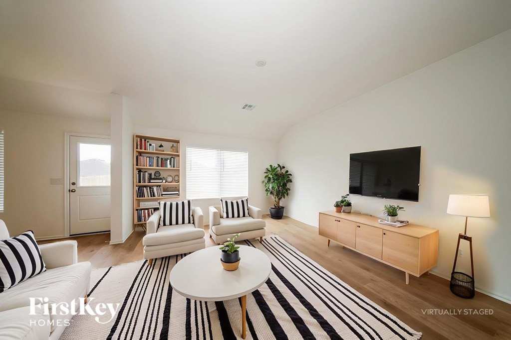 A living room with a white sofa, a black and white striped rug, a wooden coffee table, a flat screen TV, and a bookshelf with books and plants.