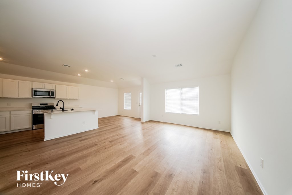A spacious empty room with wooden floors and a kitchen area in the background.
