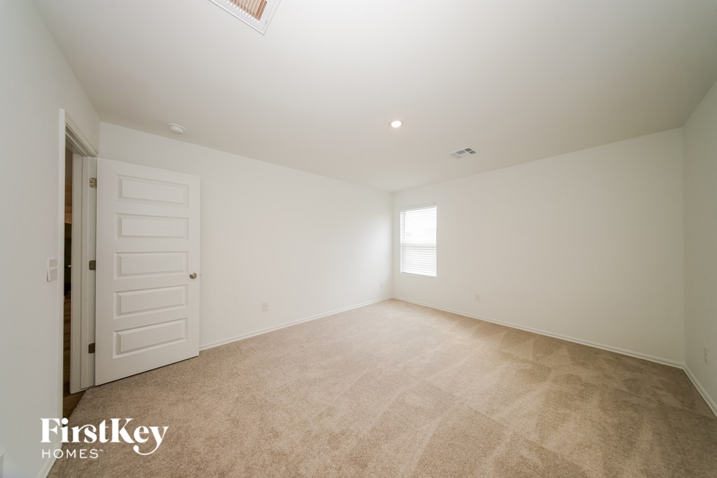 A spacious empty room with a carpeted floor and a door on the left side.