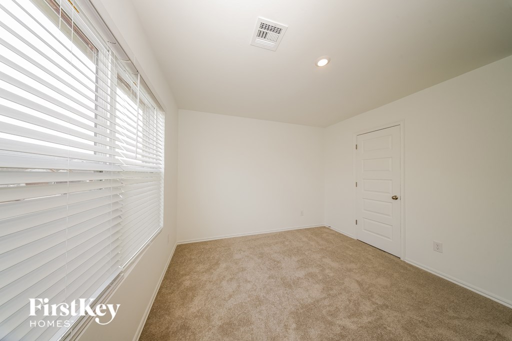 A room with a carpeted floor, a white door, and a window with blinds.