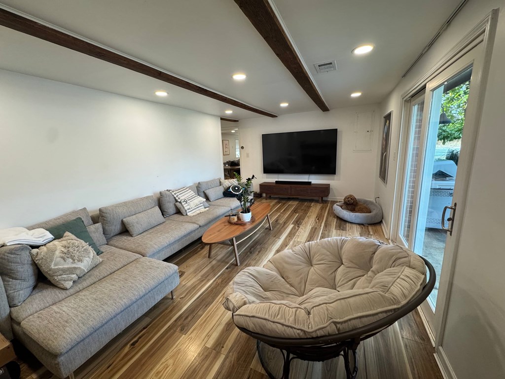 A modern living room with a grey sofa, a round ottoman, and a flat screen TV mounted on the wall.