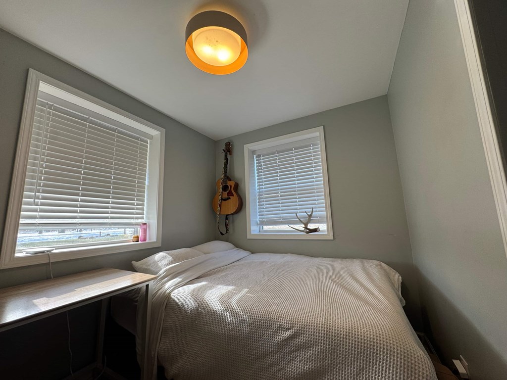 A bedroom with a bed, a window with blinds, and a guitar hanging on the wall.