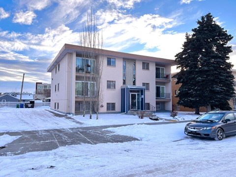 A car is parked in front of a building with a tree to the right.
