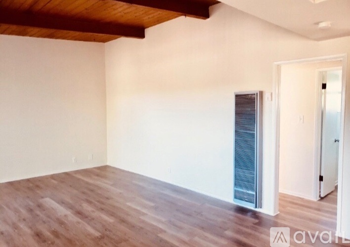 A room with wooden floors and white walls, with a door on the right side.