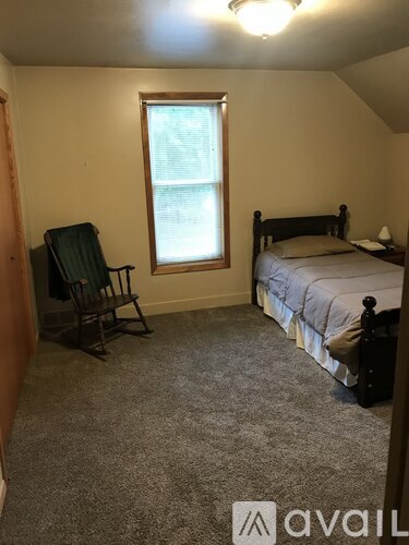 A bedroom with a bed, chair, and window.