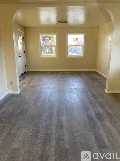 A spacious room with grey flooring and two windows.