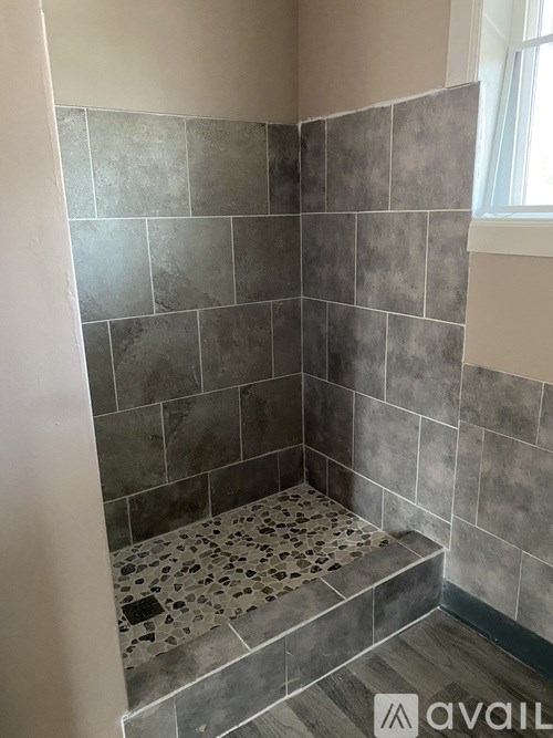 A bathroom with grey tiles and a window.