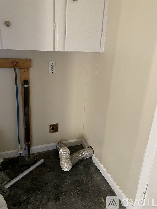 A room with white cabinets and a pipe on the floor.