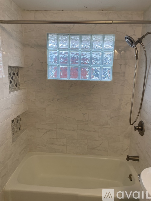 A bathroom with a tub, shower, and a window with frosted glass.
