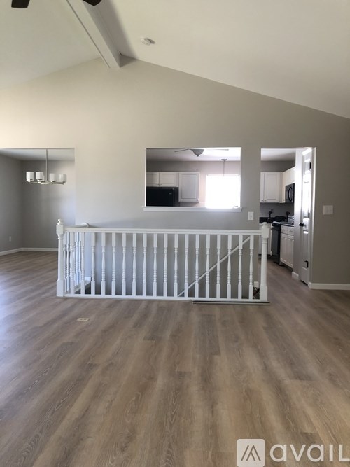 A baby crib sits in the middle of a spacious, empty room with light wood flooring.