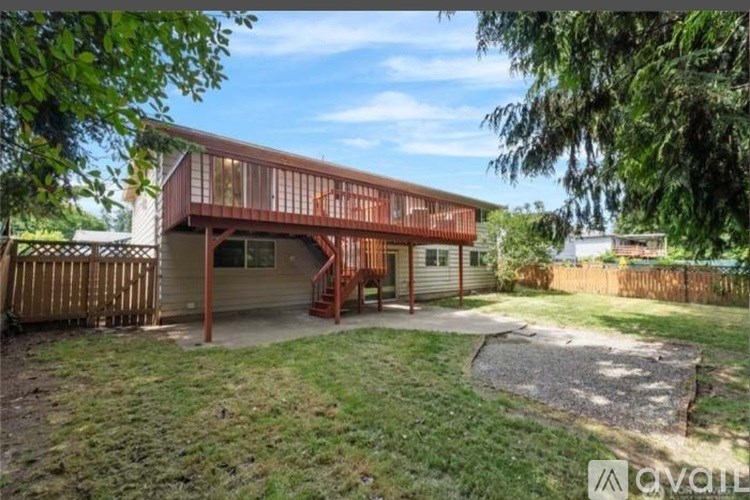 A house with a wooden deck and a garage is surrounded by a fence and trees.