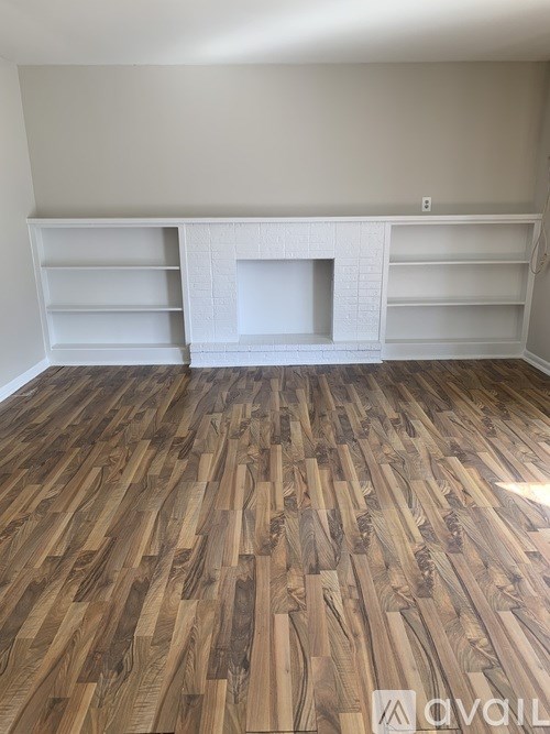 A room with wooden flooring and a white fireplace.