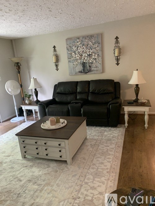 A living room with a black leather couch, a coffee table, and a painting on the wall.
