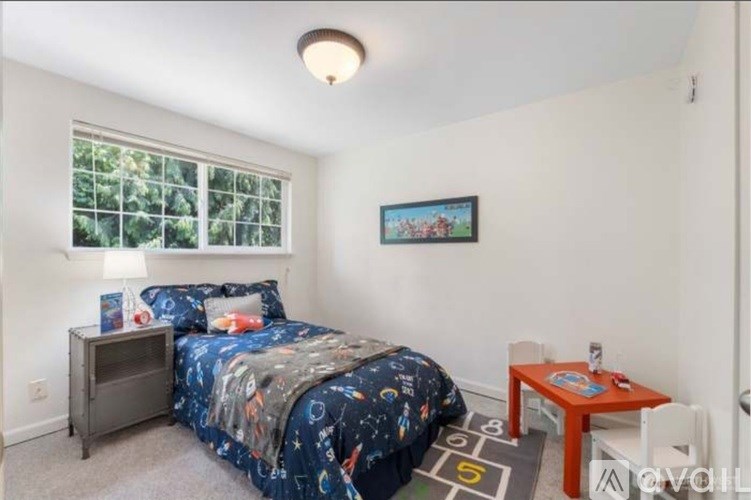 A bedroom with a bed, a small table, and a window with a view of trees.