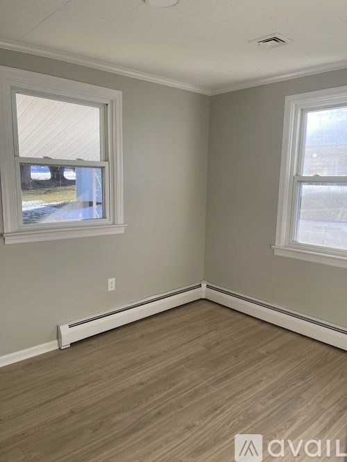 A room with light grey walls and wooden flooring with two windows.