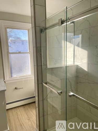 A glass shower door in a bathroom with a window.