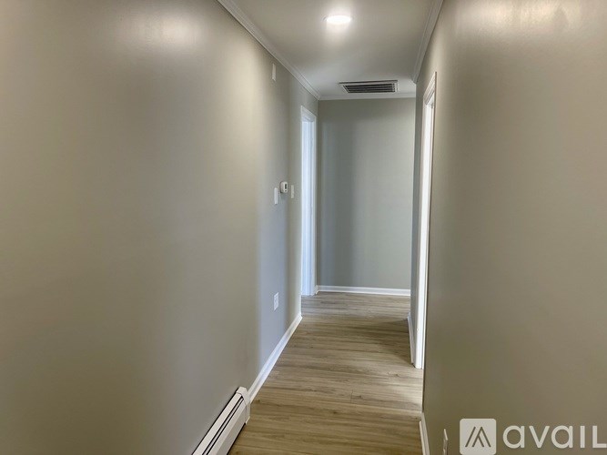 A long, narrow hallway with wood flooring and white walls.