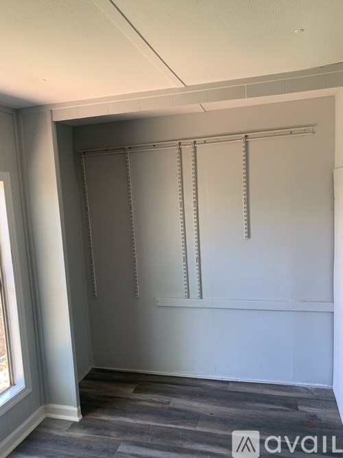 A room with a grey floor and a white wall with a window on the left side.
