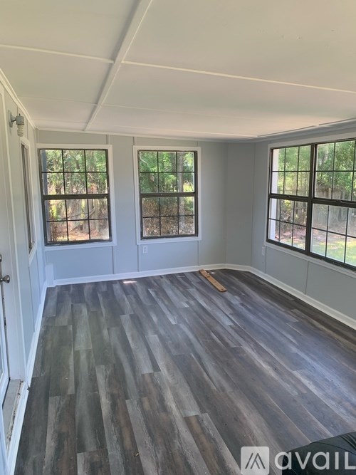 A room with wooden flooring and three windows.