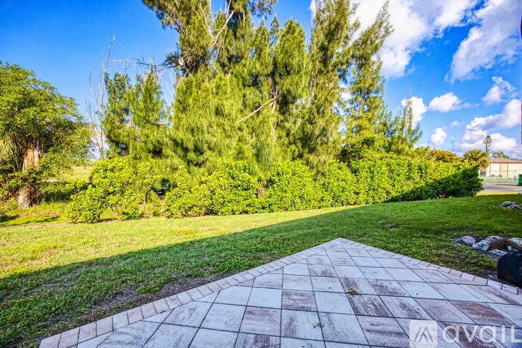 A garden with a paved pathway leading to a grassy area with trees.