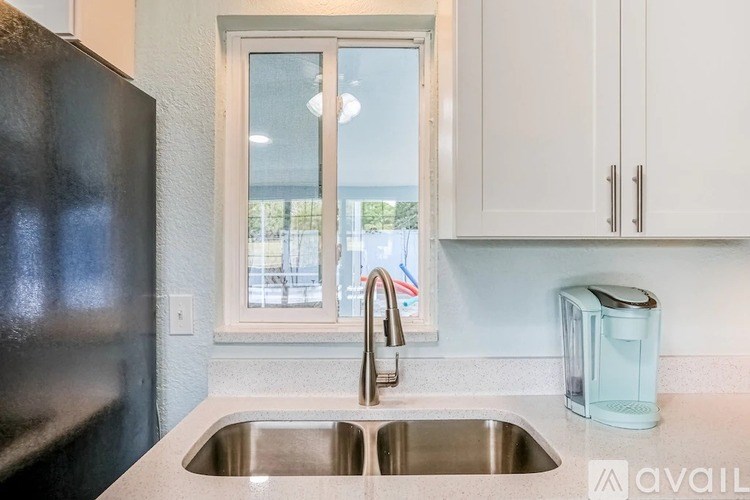 A kitchen with a black refrigerator, a sink with a faucet, and a window.