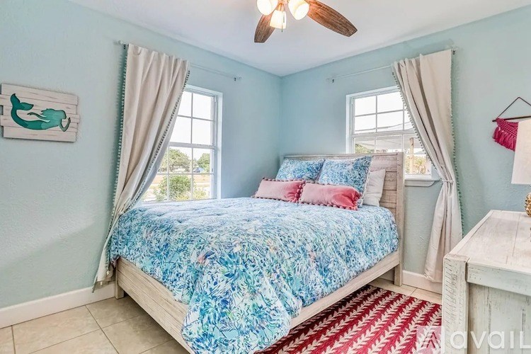 A bedroom with a bed, a ceiling fan, and a window with curtains.