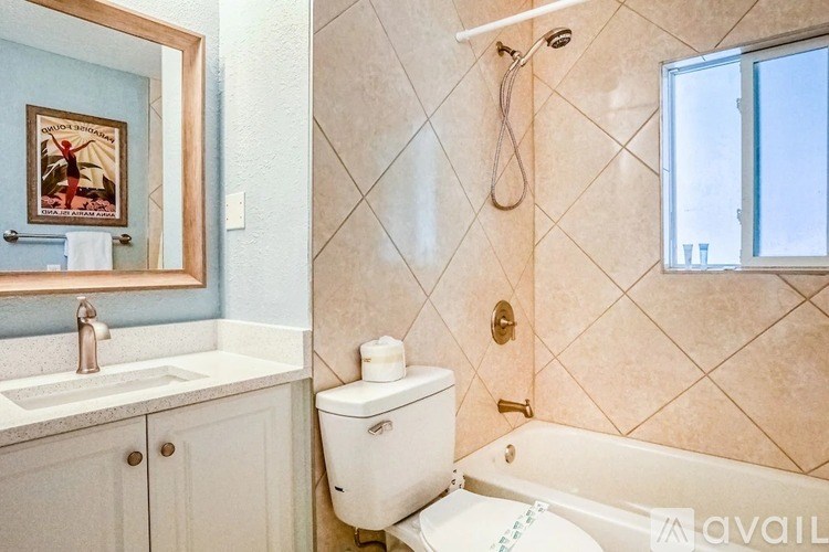 A white toilet sits in a bathroom with a sink, mirror, and bathtub.