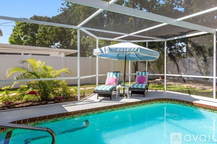 A pool with a white umbrella and two striped chairs.