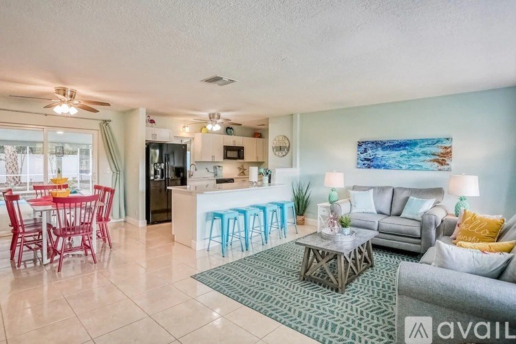A living room with a couch, a dining table with chairs, and a kitchen area in the background.