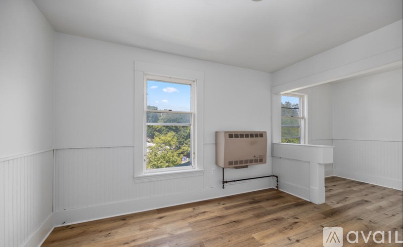 A room with white walls and wooden flooring, two windows, and a white radiator.
