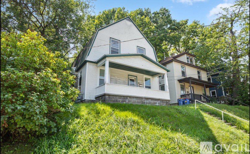 A white house with a green roof is surrounded by trees and grass.