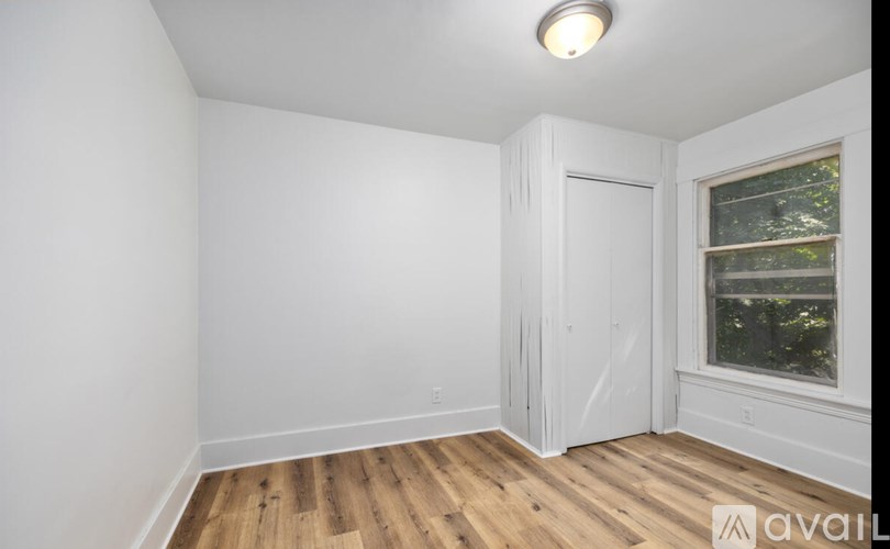 A room with wooden floors and a window showing trees outside.