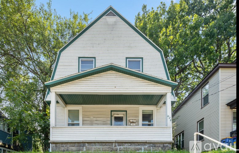 A white house with a green roof is surrounded by trees.