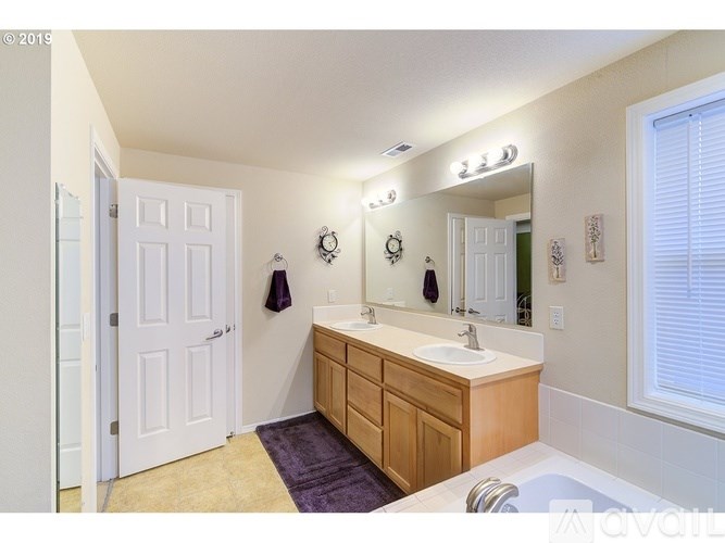 A bathroom with a white door, a vanity with a sink, and a purple rug.