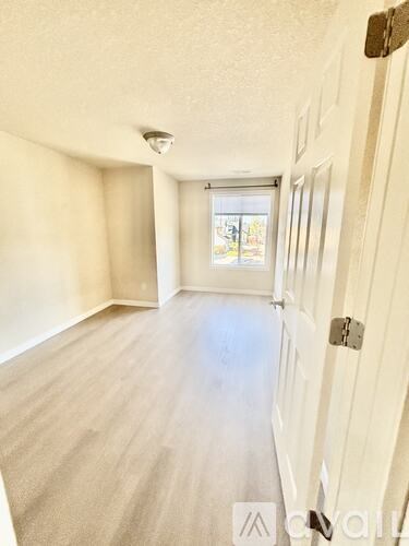 A room with a white door and a window with a view of a fence and trees outside.