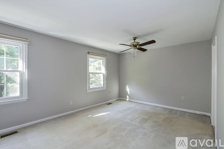 A room with a ceiling fan and two windows.
