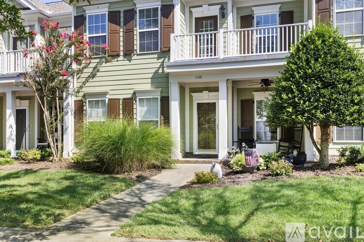 A green two-story building with a balcony and a tree in front.