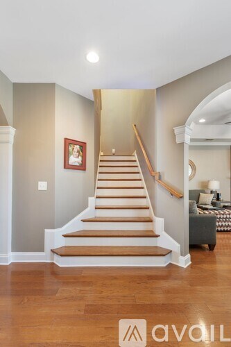 A staircase with wooden steps and a light brown runner leads up to a landing with a couch and a lamp.