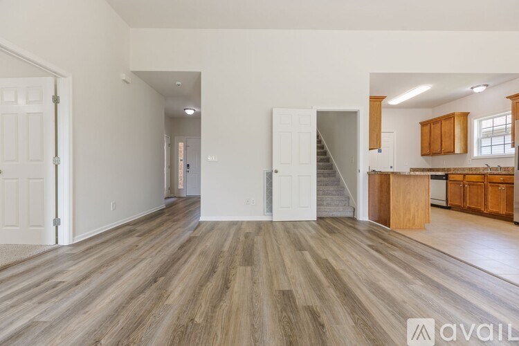 A spacious living room with wooden flooring and a kitchen area in the background.