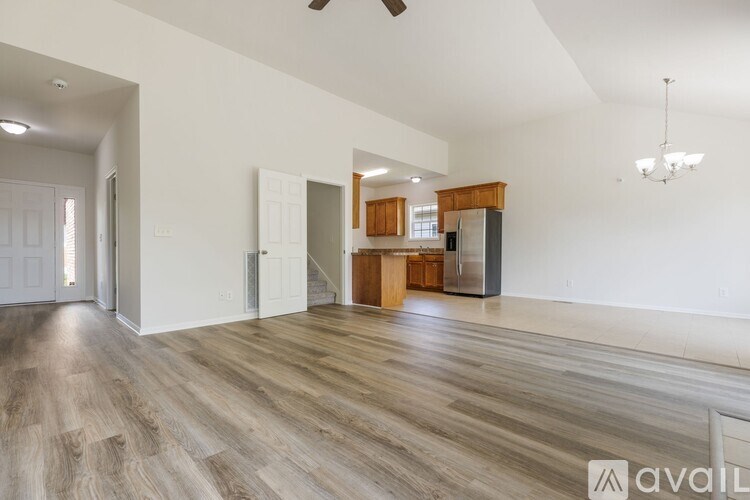 A spacious living room with wood flooring and a kitchen area in the background.